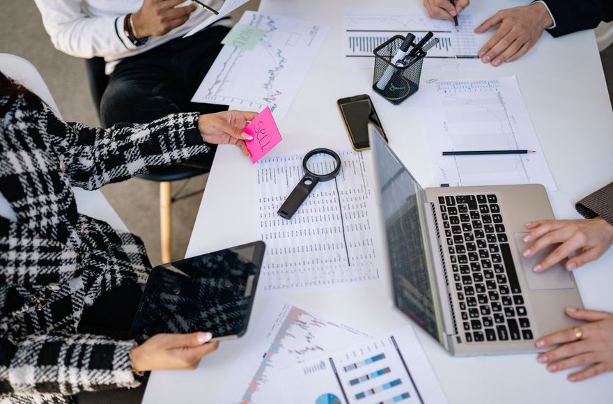Reunión de trabajo sobre una mesa con informes, gráficas y un ordenador portátil.